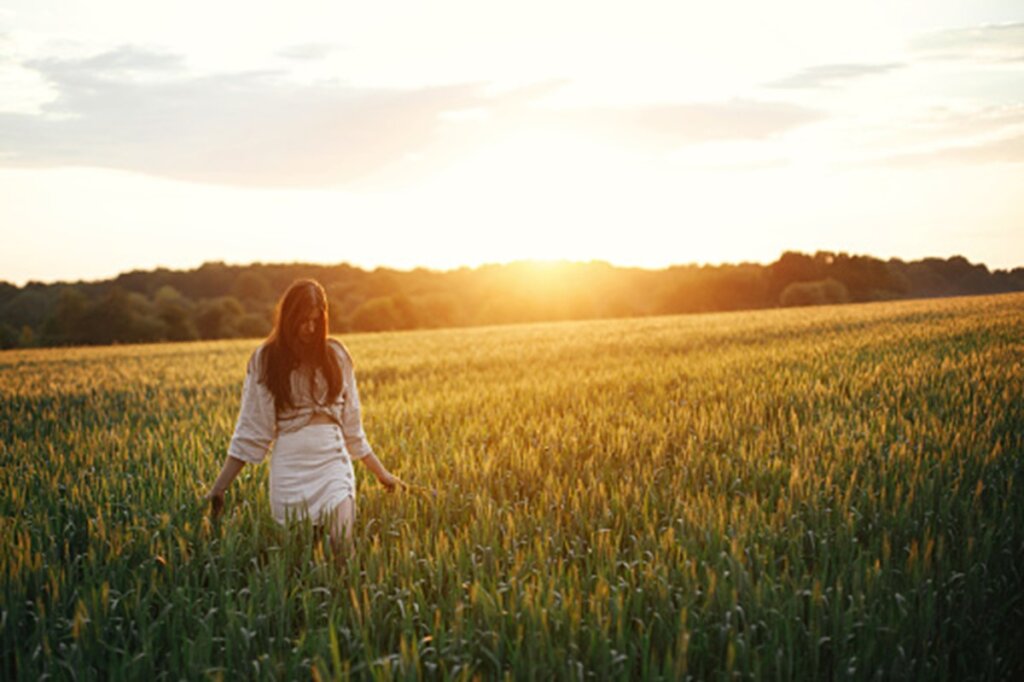 Mujer caminando tranquila en un campo de trigo al atardecer simbolizando la paz interior y la libertad.