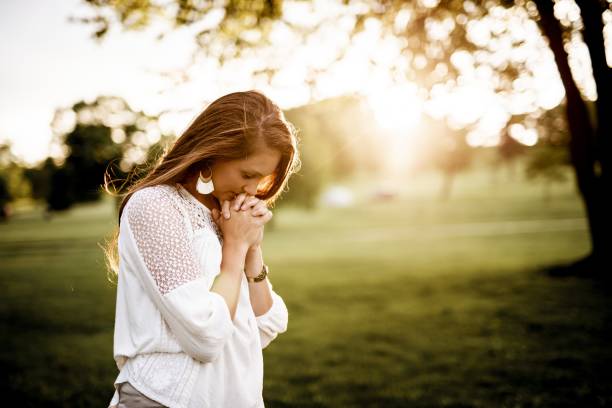 Mujer joven orando con fe en un parque para encontrar consuelo y fortaleza espiritual según las enseñanzas de Jesús.